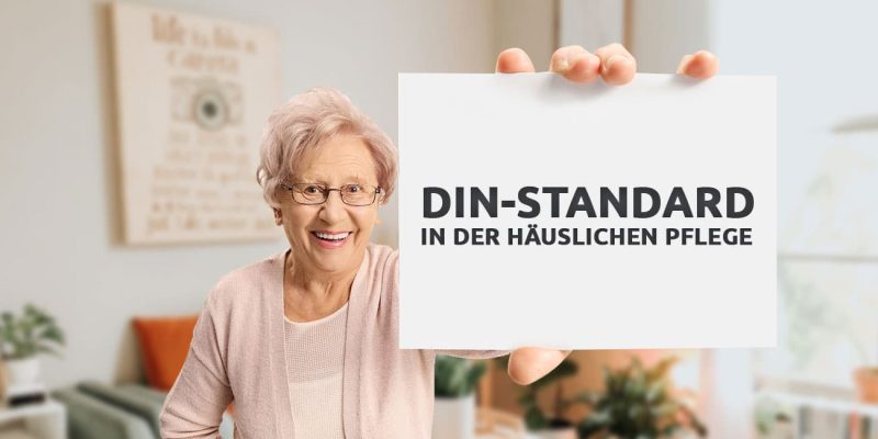 Eine lächelnde Seniorin, die ein Schild mit der Aufschrift "DIN-Standard in der häuslichen Pflege" hochhält