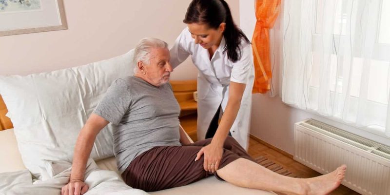 Eine Pflegekraft hilft einem Senior beim Aufstehen aus dem Bett