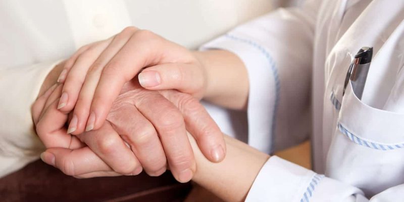 Eine Pflegekraft hält die Hand eines Seniors in ihren Händen