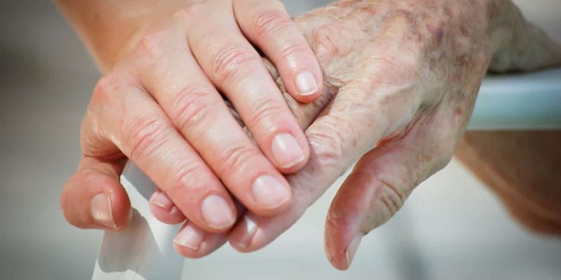 Eine Hand liegt auf der Hand eines Seniors