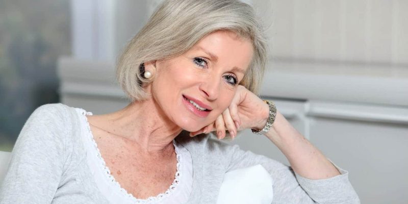 Eine lächelnde Seniorin, die auf der Couch sitzt und in die Kamera schaut