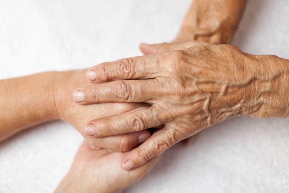 Die Hände einer Seniorin, die die Hände einer Pflegerin umschließen