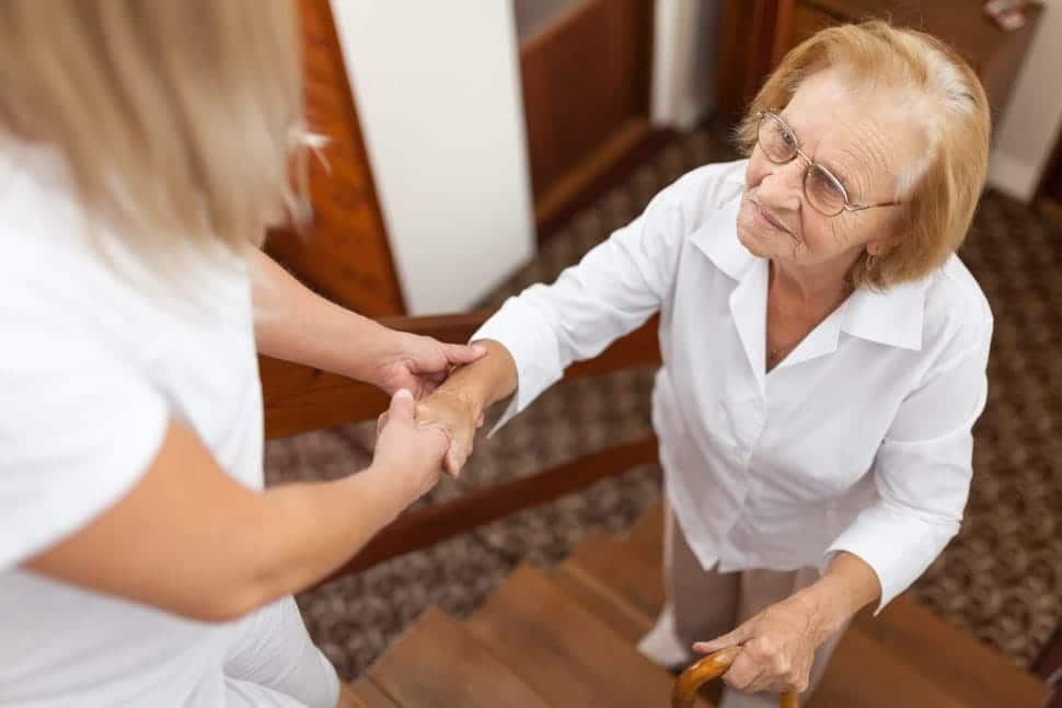 Eine Pflegerin hilft einer Seniorin beim Treppensteigen